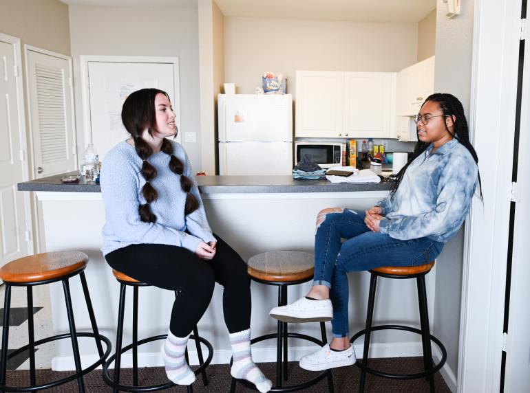 two female sitting on kitchen barstools talking
