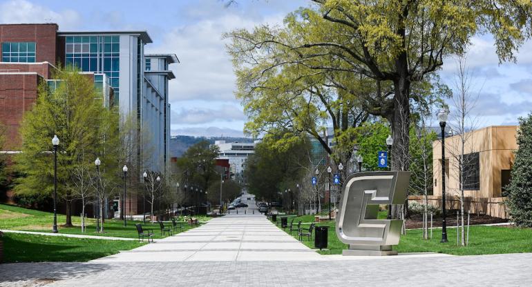 A view of the tree-lined Vine Street Pedestrian Mall on the UTC Campus, including the stainless-steel "Power C" logo sculpture, Derthick Hall and the UTC Library, with the Unum building in the background.
