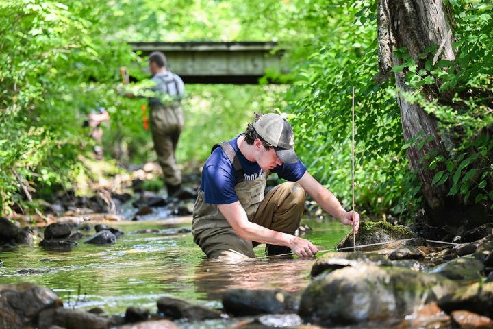 A UTC student measures stream depth in a local creek