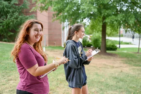 Two female forensic anthropology students outside taking notes.